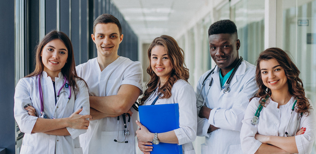 Five smiling medical students in white coats with stethoscopes